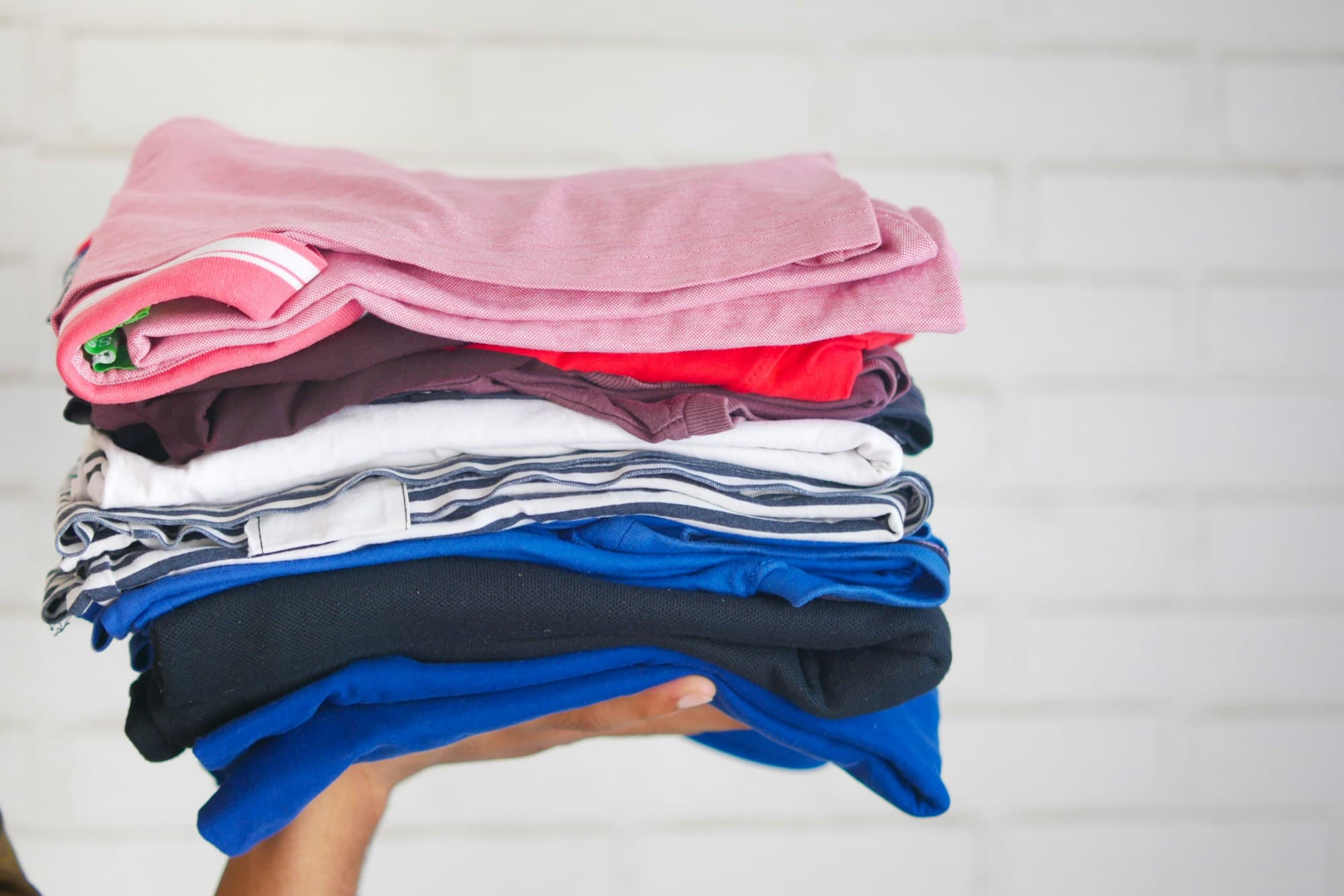 A tall stack of freshly folded, brightly coloured laundry carried in both arms